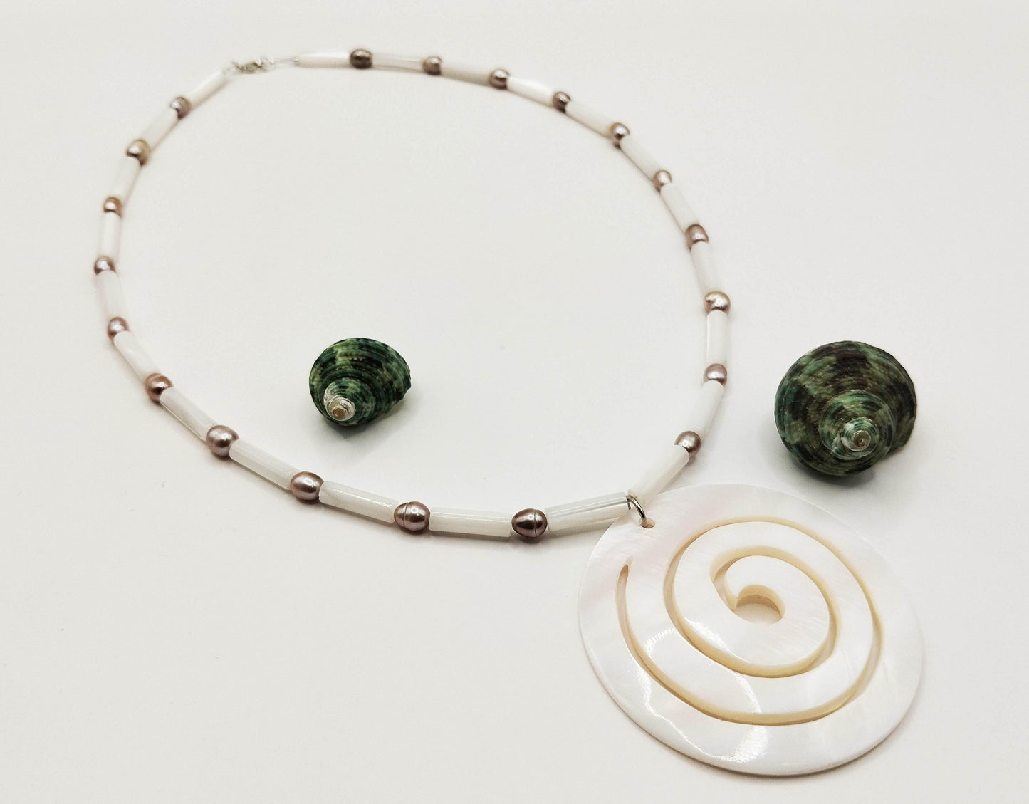 Κολιέ με φίλντισι και μαύρα μαργαριτάρια σε ατσαλόσυρμα με κούμπωμα ασήμι 925.
Οι φιλντισένιες χάντρες εναλλάσσονται με μαύρα μαργαριτάρια. Ένα μεγάλο μενταγιόν από φίλντισι σε σχήμα σπείρας κρέμεται μπροστά.
Εντυπωσιακό, καλοκαιρινό κομμάτι.