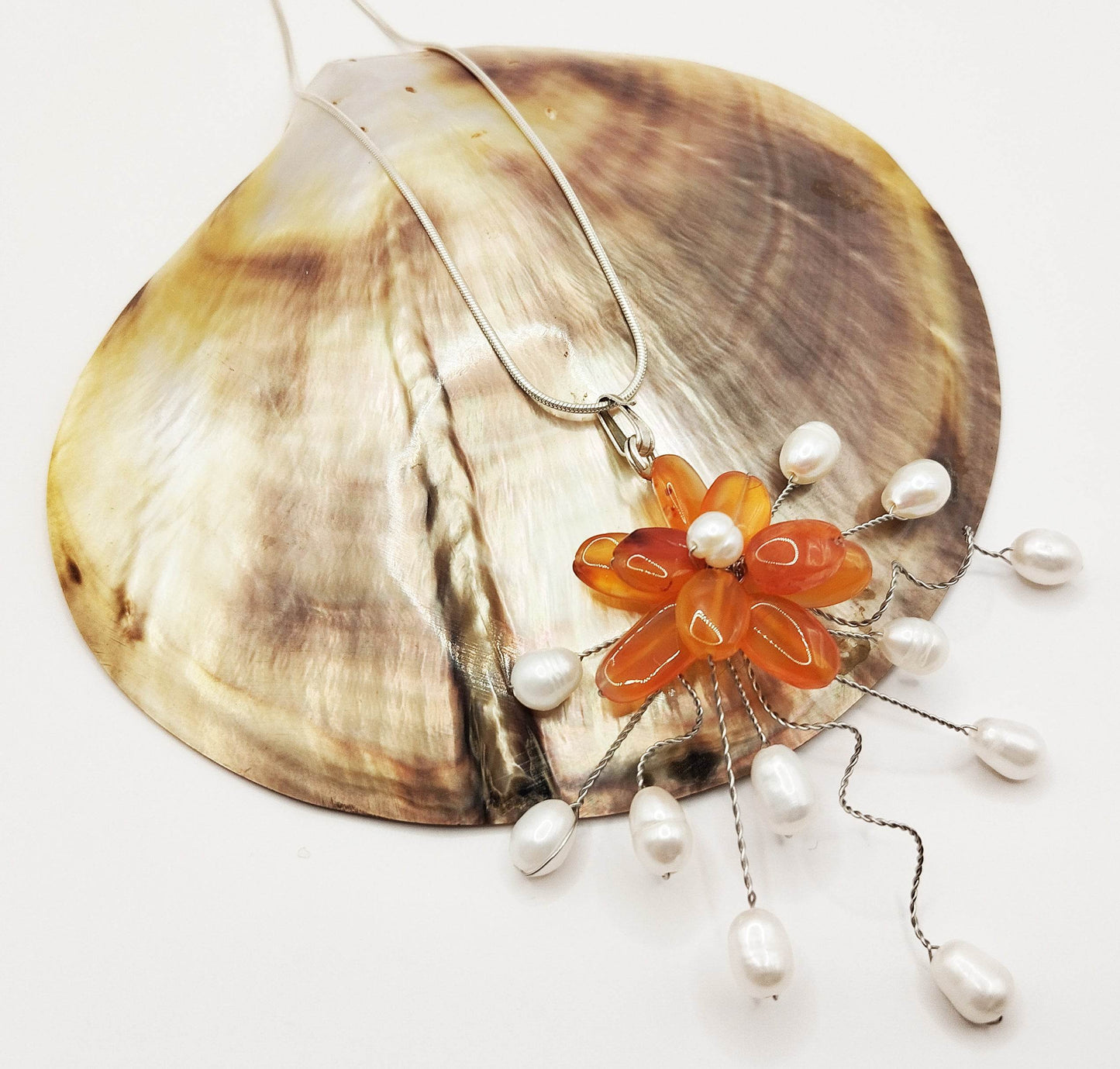 Ασημένιο κολιέ με μενταγιόν που αποτελείται από ένα λουλούδι φτιαγμένο από καρνεόλη και μαργαριτάρι και 11 επιπλέον μαργαριτάρια γύρω από το λουλούδι.