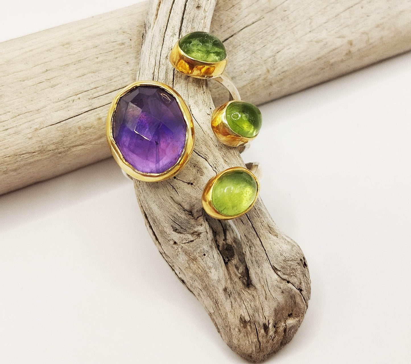 Ασημένιο δαχτυλίδι με επίχρυσες λεπτομέρειες και οβάλ ημι-πολύτιμους λίθους: μια μεγάλη πέτρα από μωβ αμέθυστο και τρεις μικρότερες από πράσινο περίδοτο.
Πρόκειται για εντυπωσιακό κομμάτι, ιδανικό για ιδιαίτερες περιστάσεις ή για όποτε αισθάνεστε την ανάγκη να φορέσετε κάτι που να τραβάει τα βλέμματα.