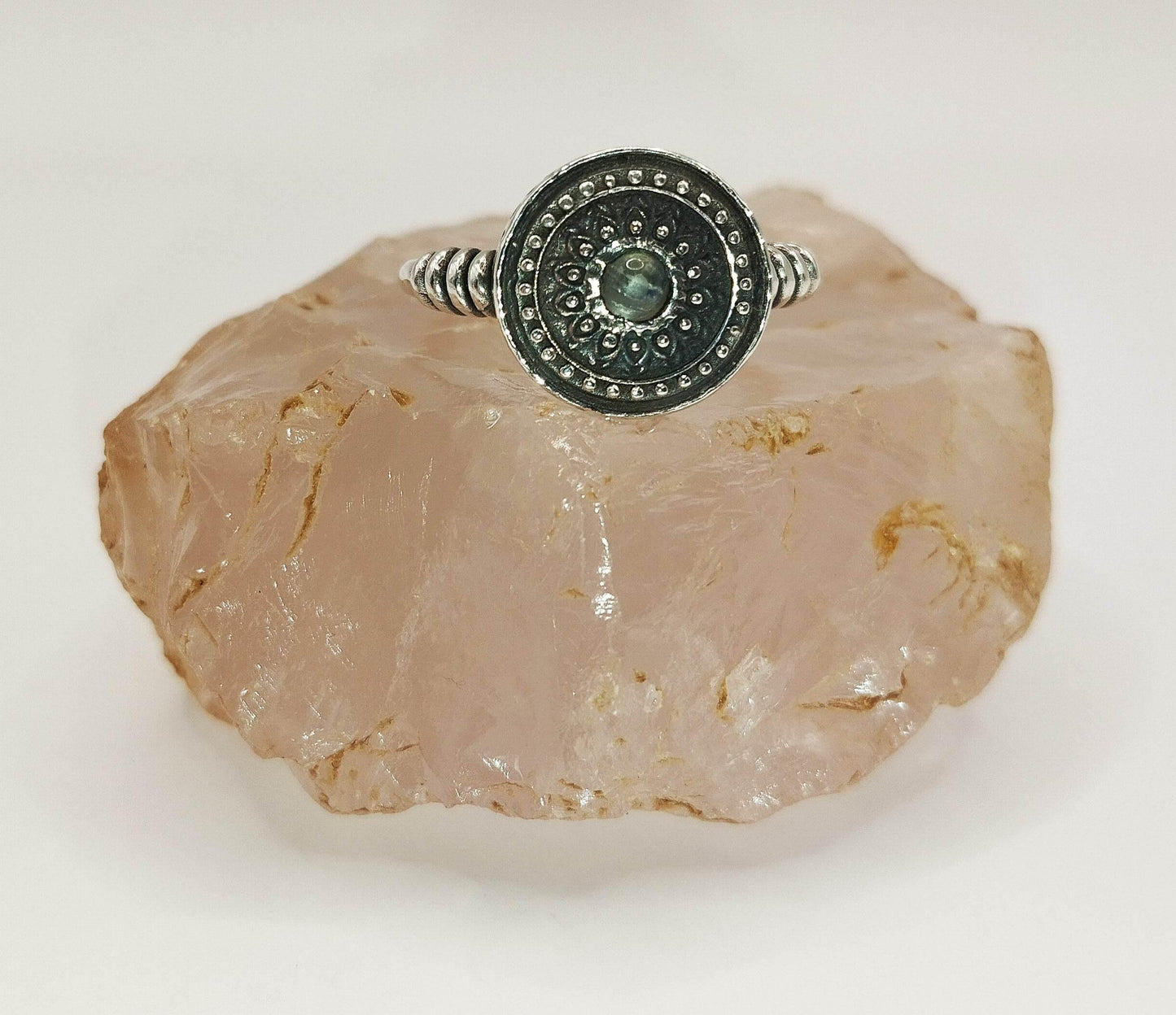 Ασημένιο στρογγυλό δαχτυλίδι με μια μικρή φεγγαρόπετρα στη μέση.
Γύρω από την πετρούλα, το δαχτυλίδι είναι χαραγμένο με μικροσκοπικές βούλες.