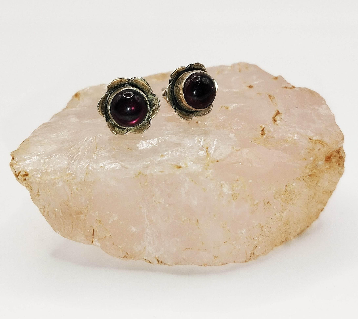 Ασημένια σκουλαρίκια καρφάκια με γρανάδα στο κέντρο ενός λουλουδιού.