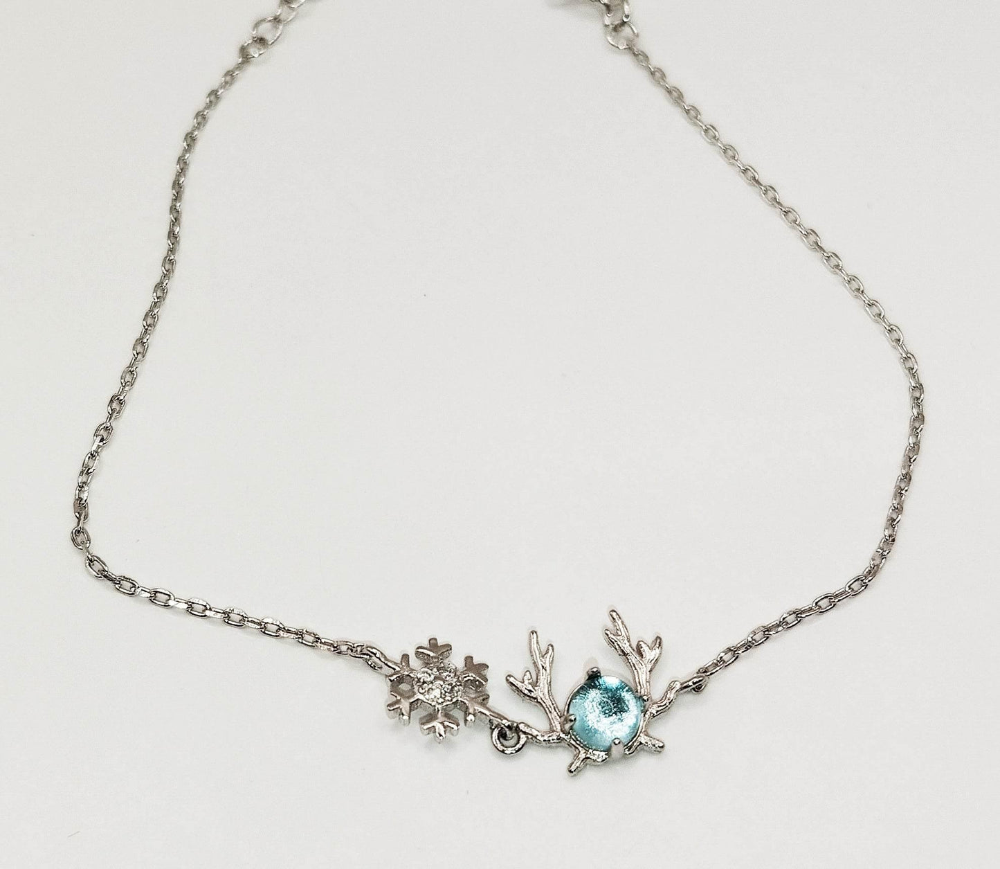 Ασημένιο βραχιόλι με γαλάζια πέτρα ζιργκόν και δύο στοιχεία χειμερινού θέματος.
Αυτό το χαριτωμένο βραχιόλι έχει επάνω μια χιονονιφάδα και ένα κεφαλάκι από ζιργκόν με κέρατα.